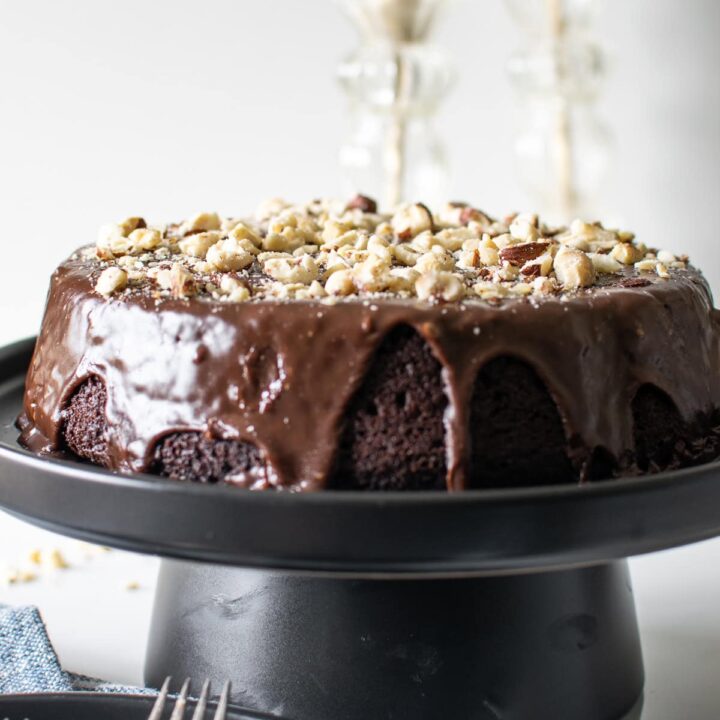 A chocolate hazelnut cake with chocolate ganache frosting sitting atop a black cake stand.