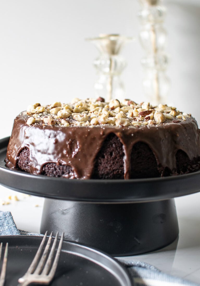 A chocolate hazelnut cake with chocolate ganache frosting sitting atop a black cake stand.