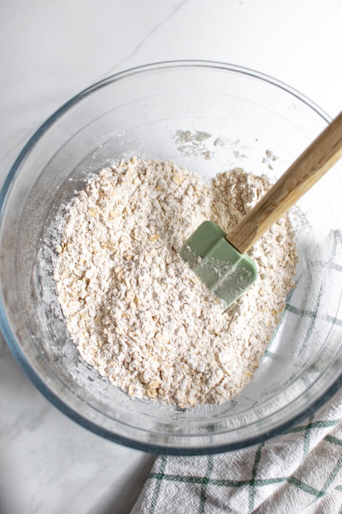 An overhead shot of the dry ingredients mixed together for oatmeal muffins, with a green spatula in the bowl.