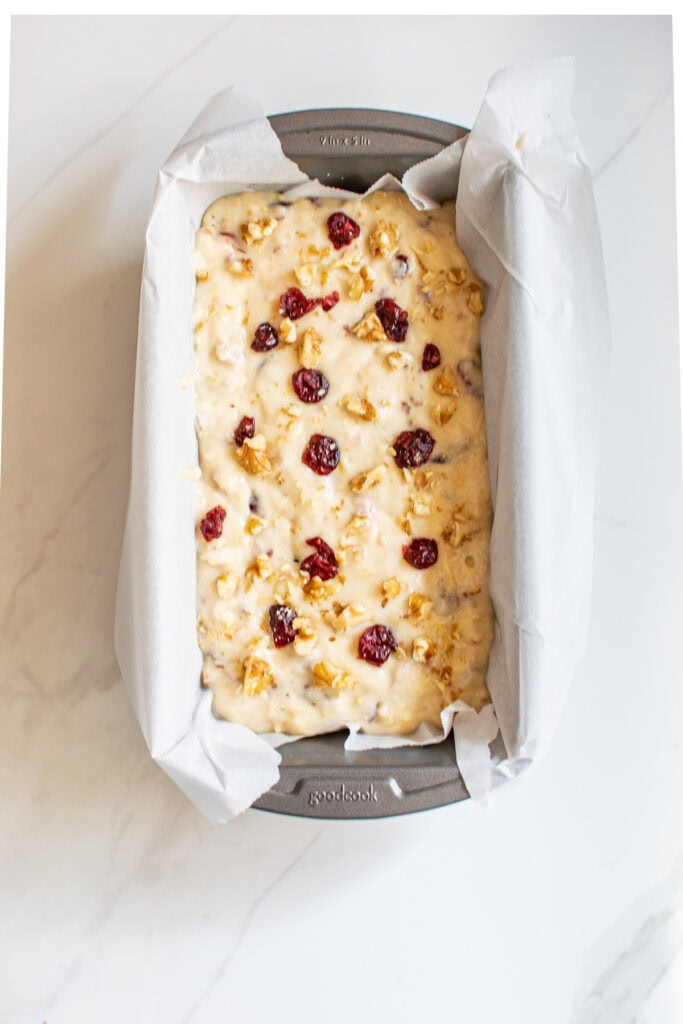 Batter for banana bread with cranberries and walnuts in a loaf pan lined with parchment.