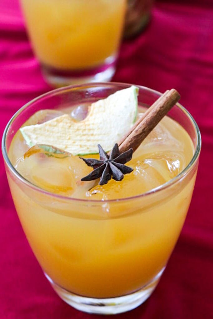 A low ball cocktail glass with and Apple Cider Cocktail topped with a cinnamon stick, dried apple slice and star anise.