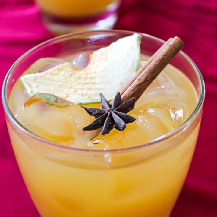 A low ball cocktail glass with and Apple Cider Rum Cocktail topped with a cinnamon stick, dried apple slice and star anise.