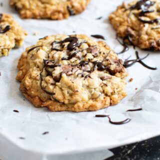 Oatmeal cookies with raisins and chocolate chips on a parchment lined baking sheet and drizzled with chocolate.