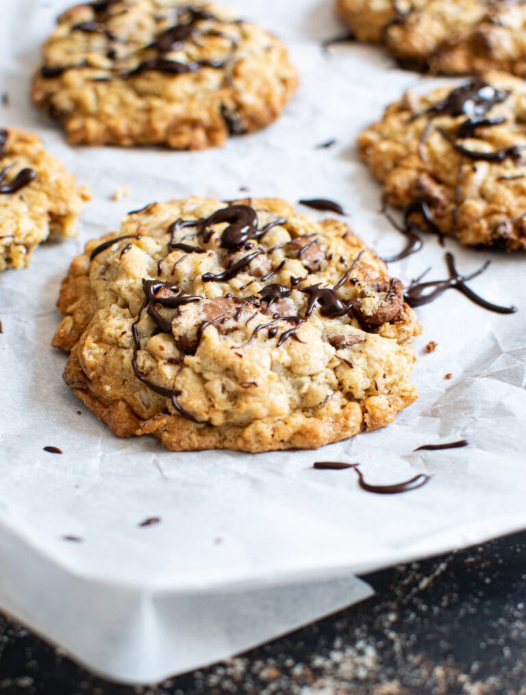 Oatmeal cookies with raisins and chocolate chips on a parchment lined baking sheet and drizzled with chocolate.