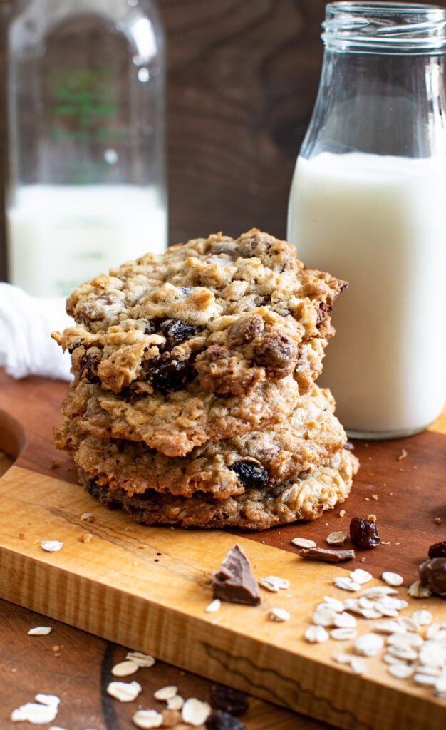 A stack of oatmeal raisin chocolate chip cookies beside a mini bottle of milk.