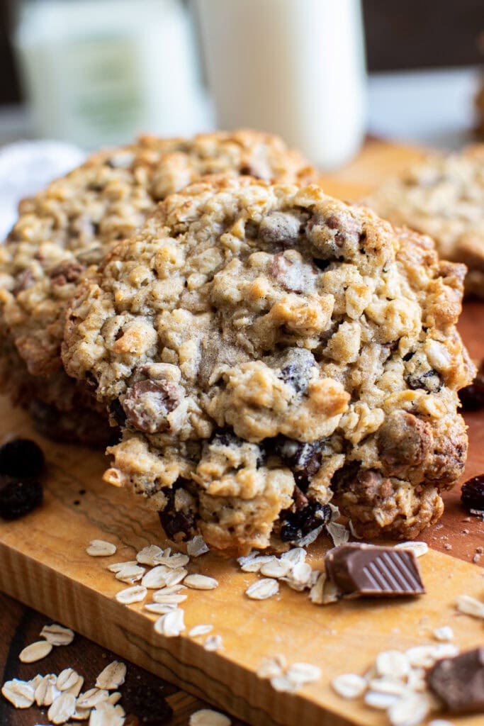 A close up picture of an oatmeal raisin cookie with chocolate chips, with oats and chunks of chocolate sprinkled around.