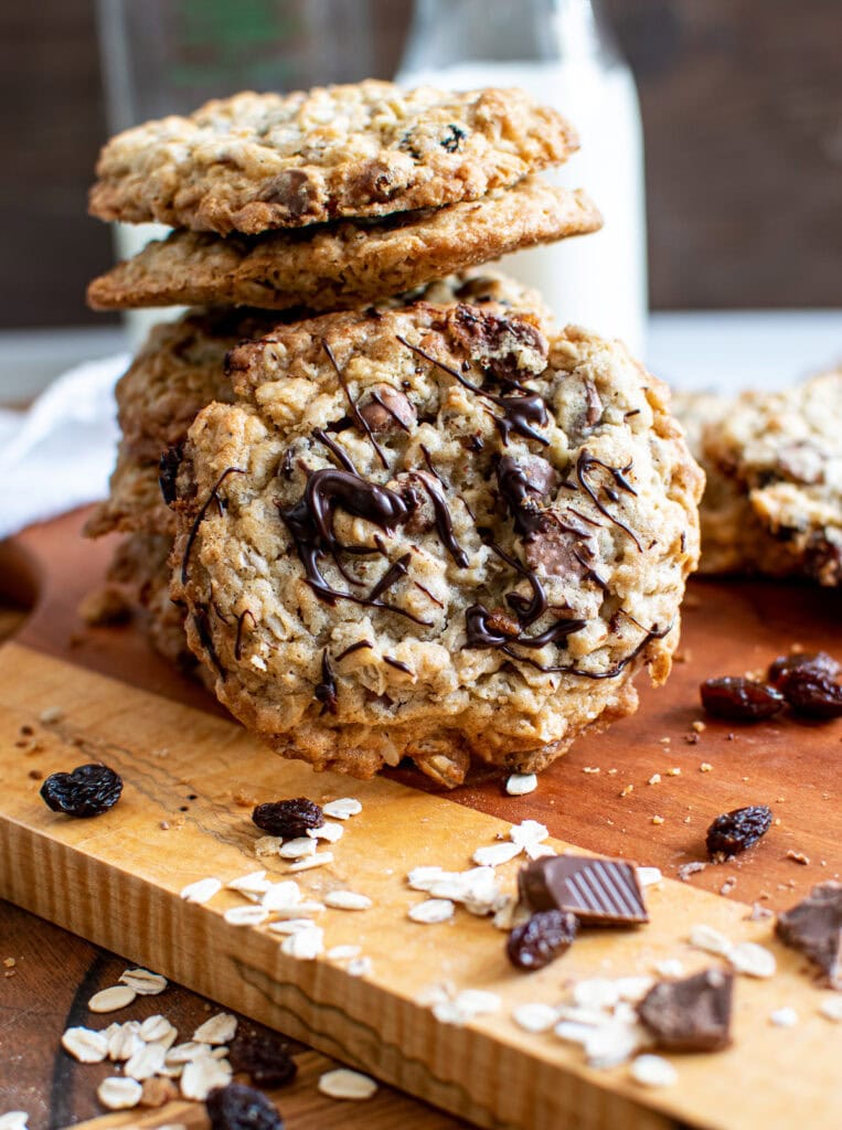 A stack of Oatmeal cookies with one leaning against the stack that has been drizzled with chocolate.