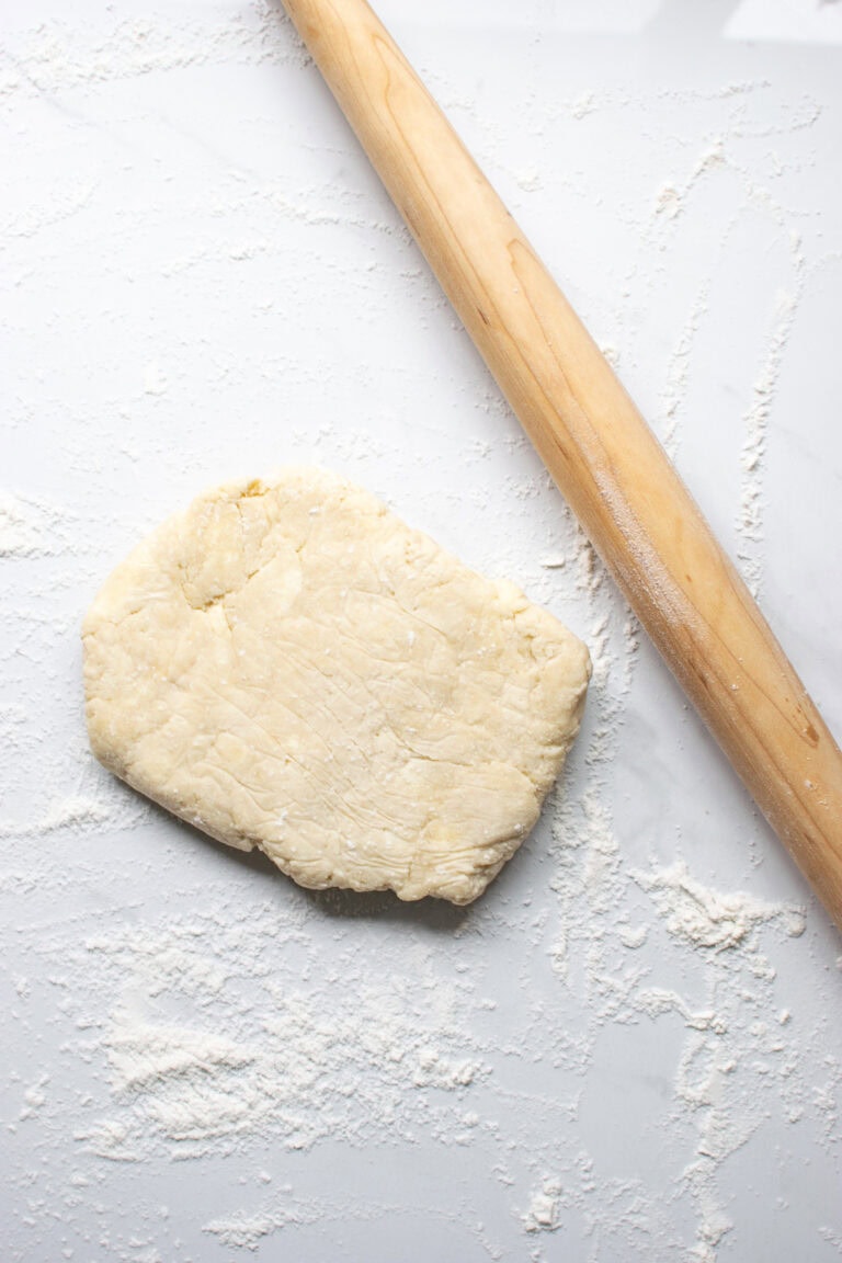 A flatted disc of pie dough ready to be rolled with a rolling pin.