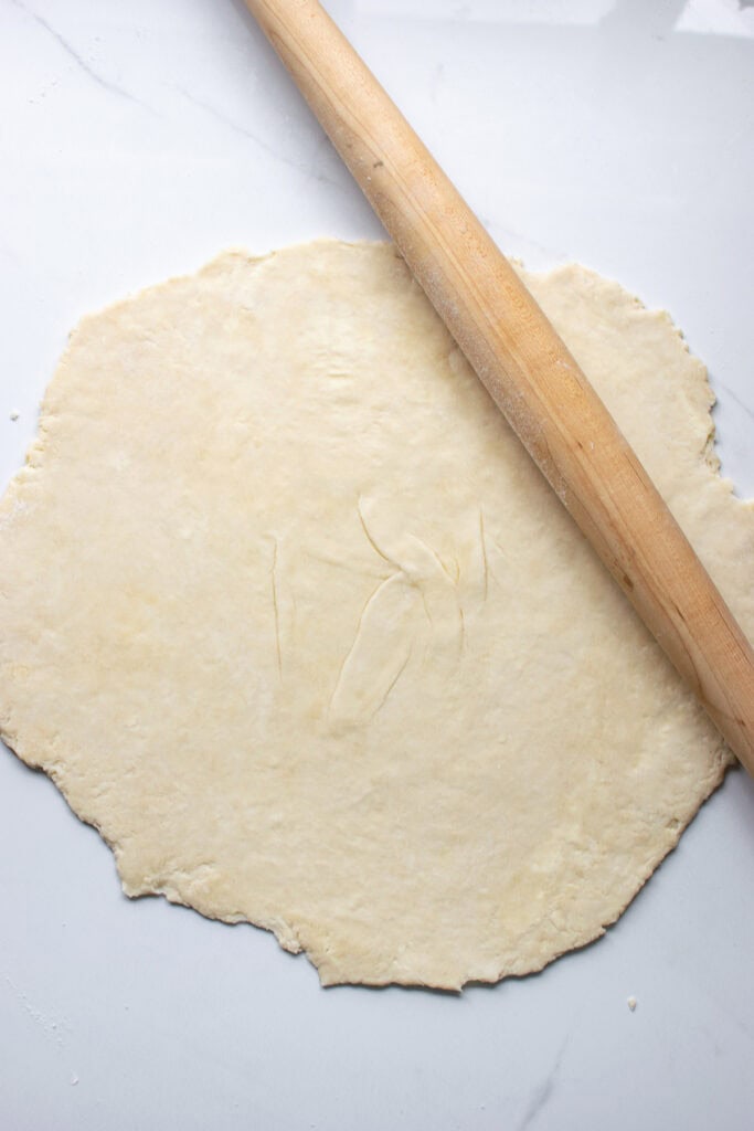 Pie dough rolled into a rough circle with a tapered rolling pin.