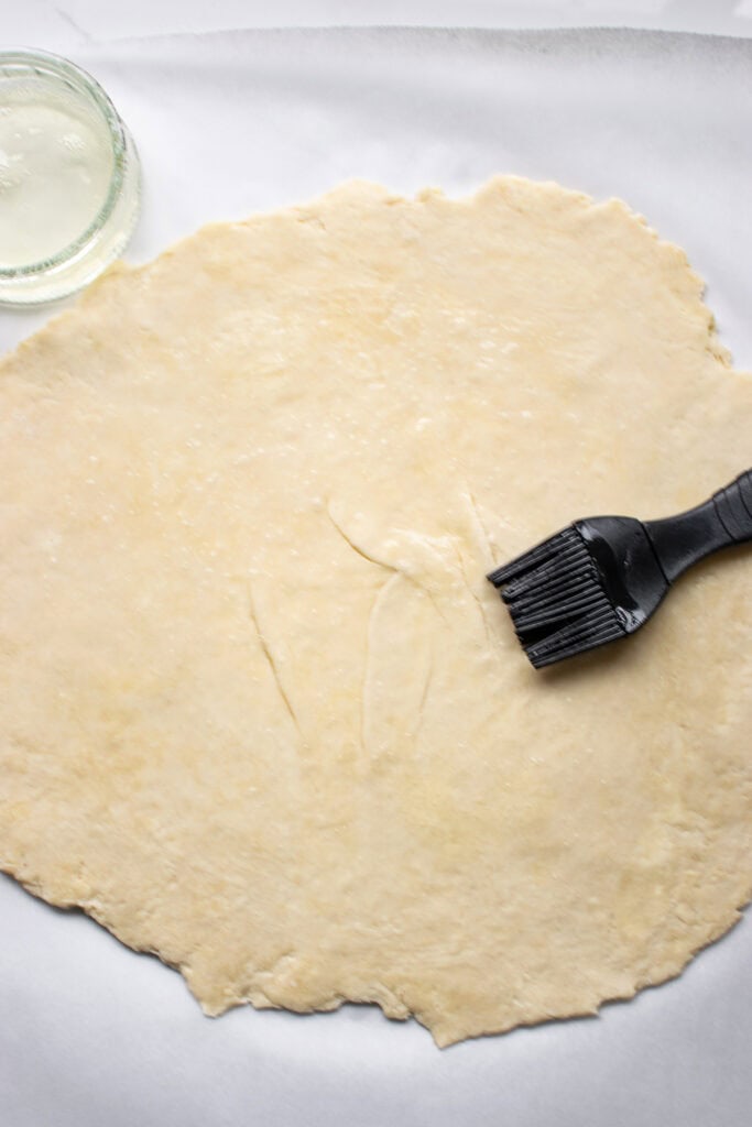 Rolled out pie dough being brushed with egg white.