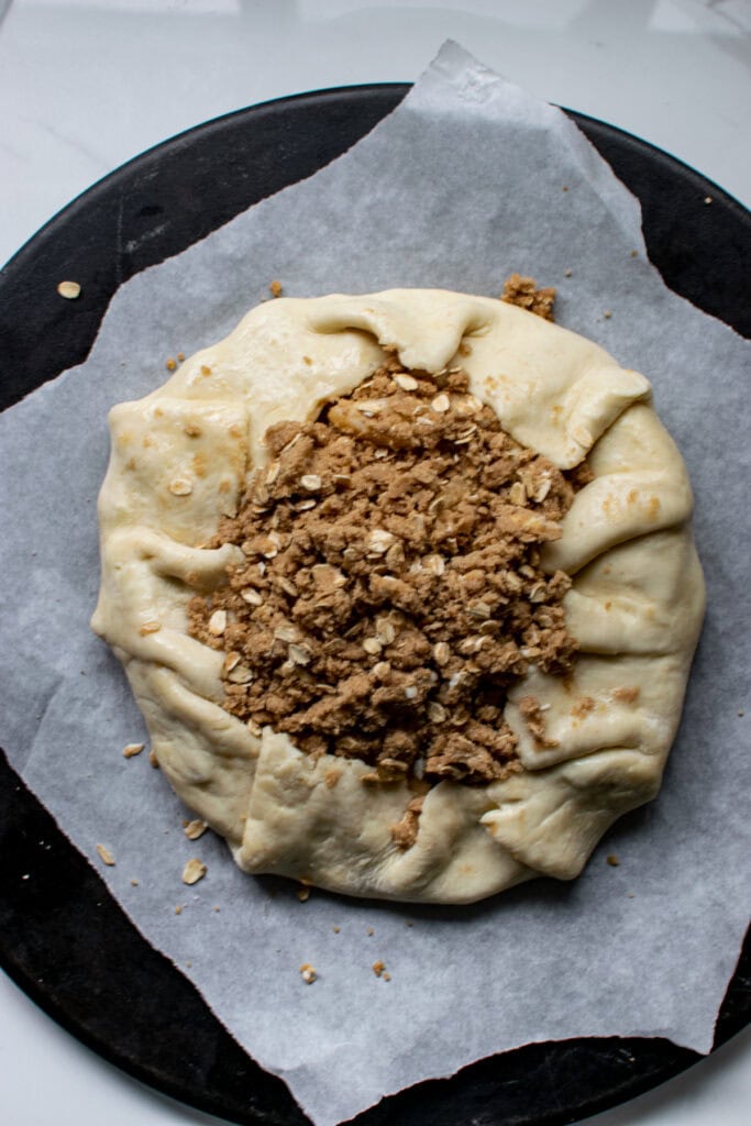 An apple ad pear galette with a crumble topping on a  parchment lined baking stone ready to go into the oven.