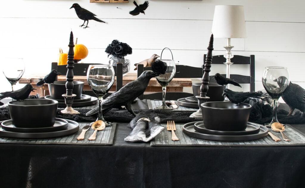 A view of a table set for a spooky Halloween party with black dishes and black crows down the centre.