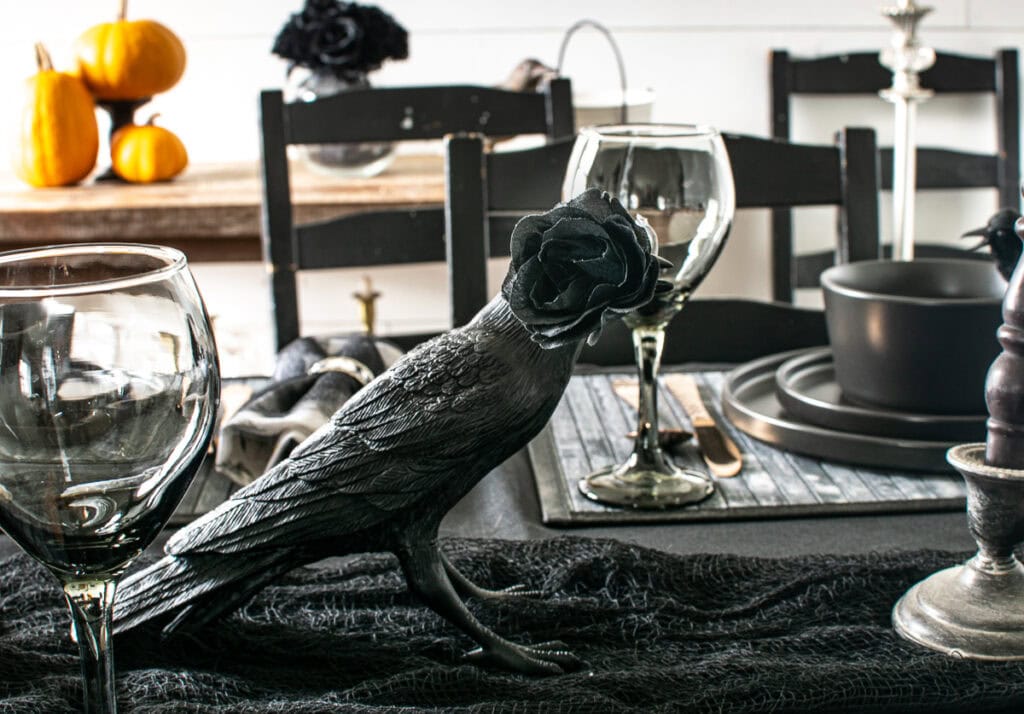 A black ceramic crow with a black rose in its' mouth on a table set for a halloween dinner party.