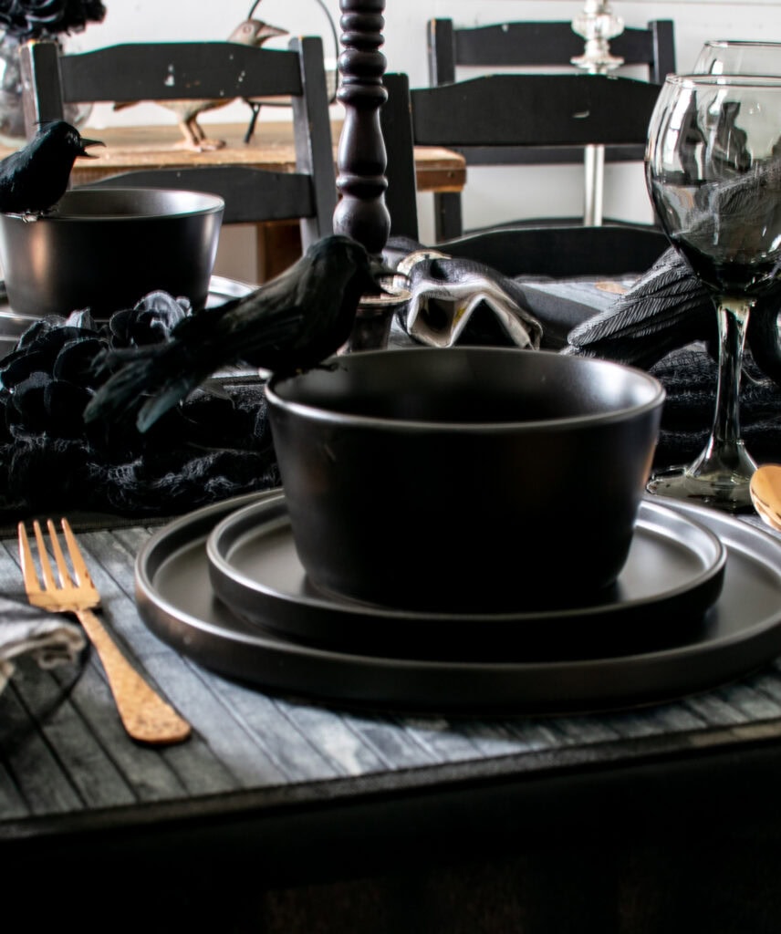 A faux black crow perched on the edge of a black soup bowl on a Halloween dinner table.