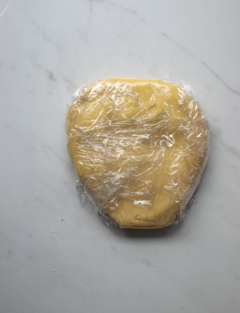 Sweet pastry dough flattened into a disc and wrapped in plastic wrap.