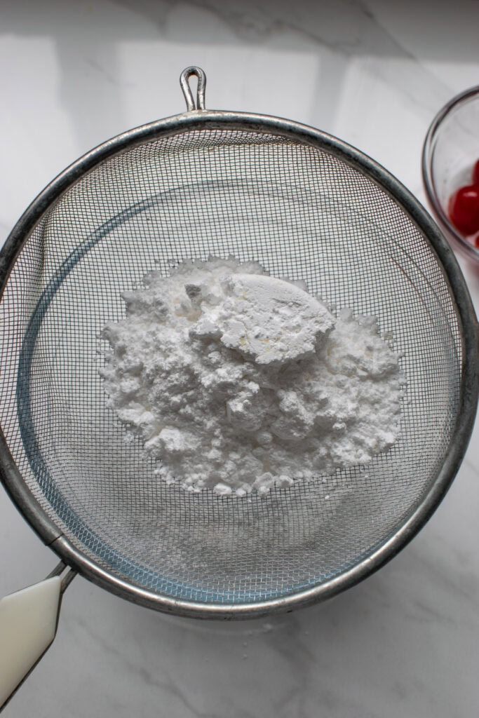 Confectioners sugar being sifted into a glass mixing bowl.