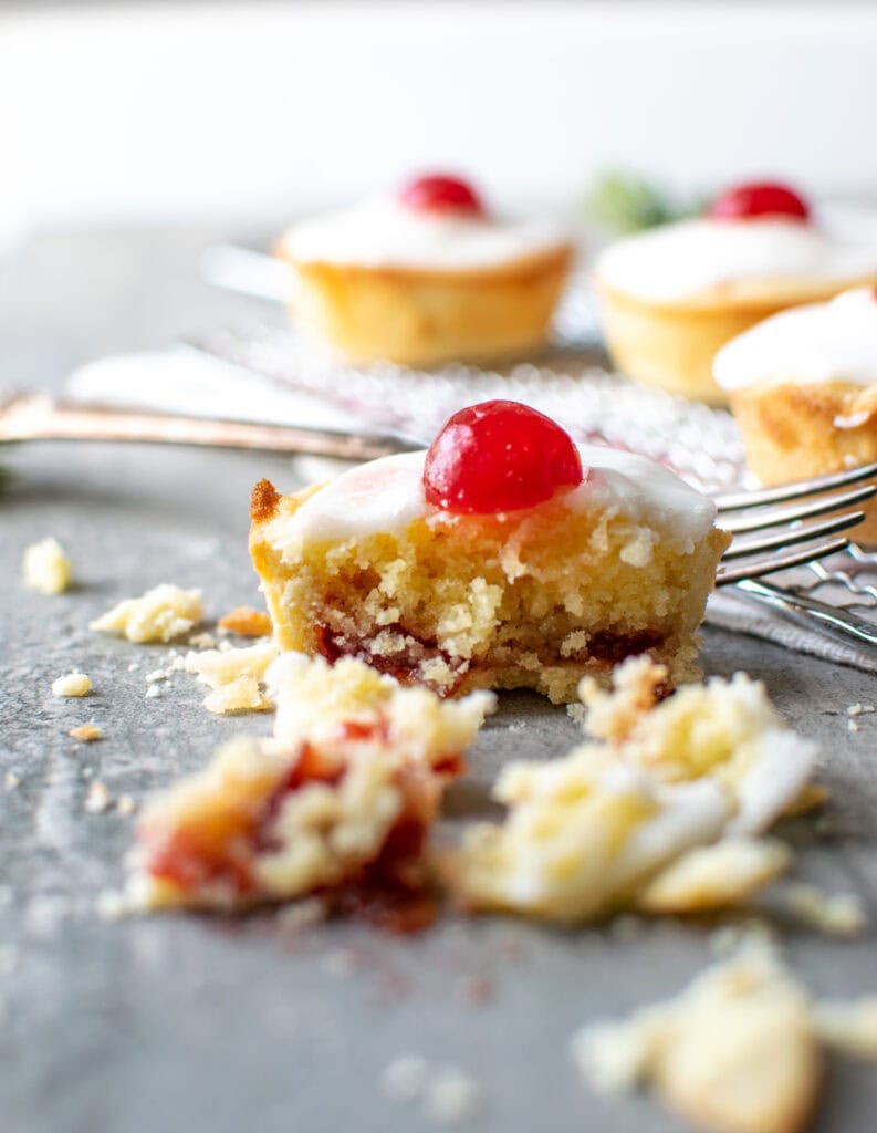 A close up of a Cherry Bakewell tart cut in half, with full tarts in the background.