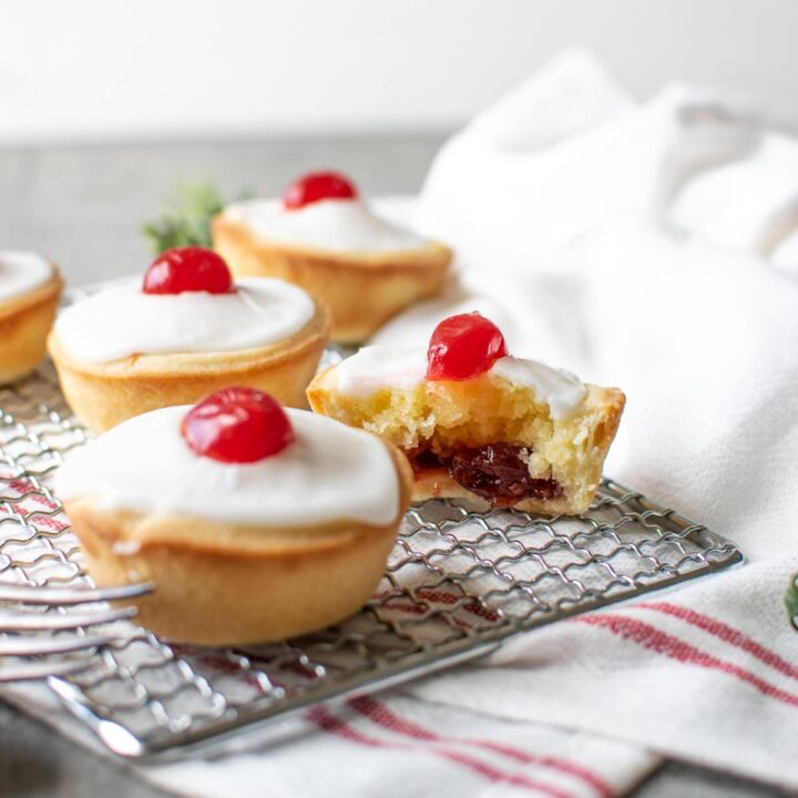 3 Cherry Bakewell tarts on a wire rack, with one cut in half showing the jam inside.