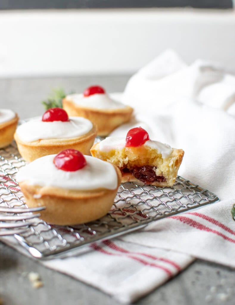 3 Cherry Bakewell tarts on a wire rack, with one cut in half showing the jam inside.