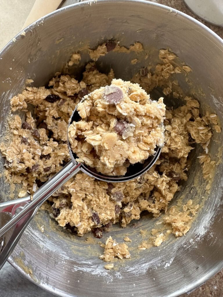 A cookie scoop with a scoop of cookie batter taken from the mixing bowl.