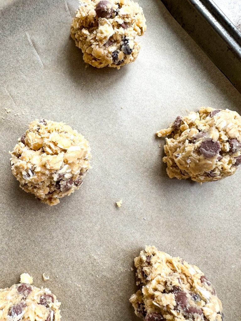 Balls of Oatmeal Chocolate Chip cookie dough on a parchment lined baking sheet.