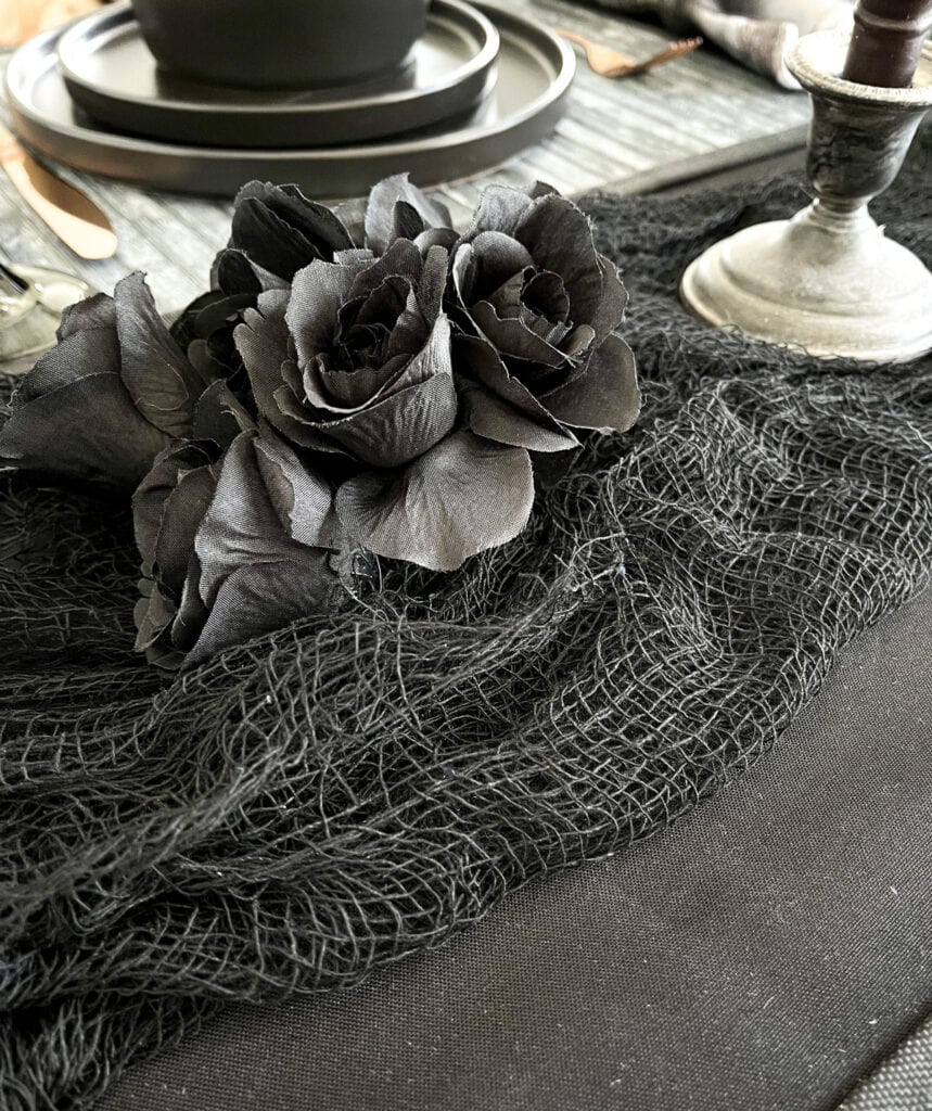 A bunch of black silk roses on a bunched up black cotton netting table runner.