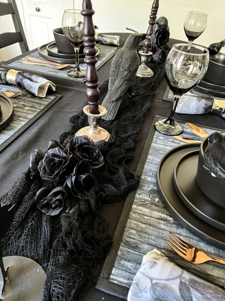 A view down the centre of a dinner table set in black with crows and black cotton netting.