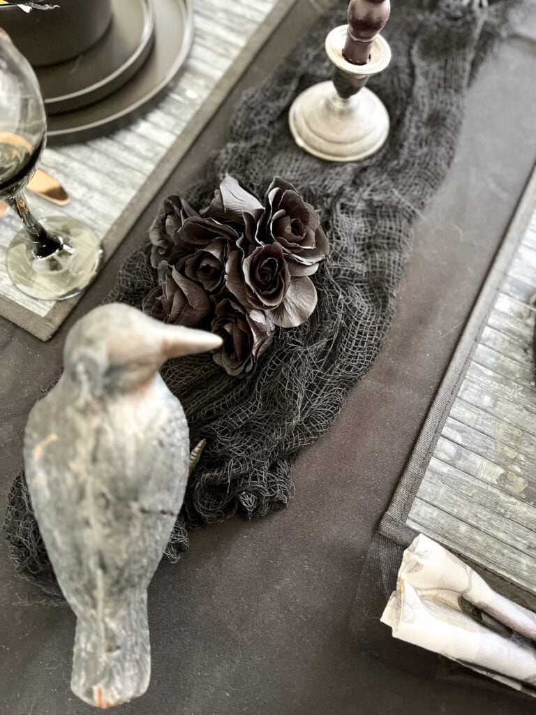 A gray grow figurine overlooking black silk roses on a dinner table set for Halloween.