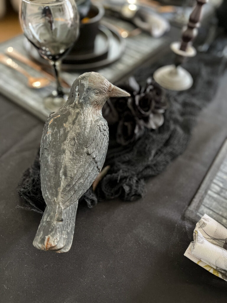 A small concrete statue of a crow on top of a table set for Halloween.