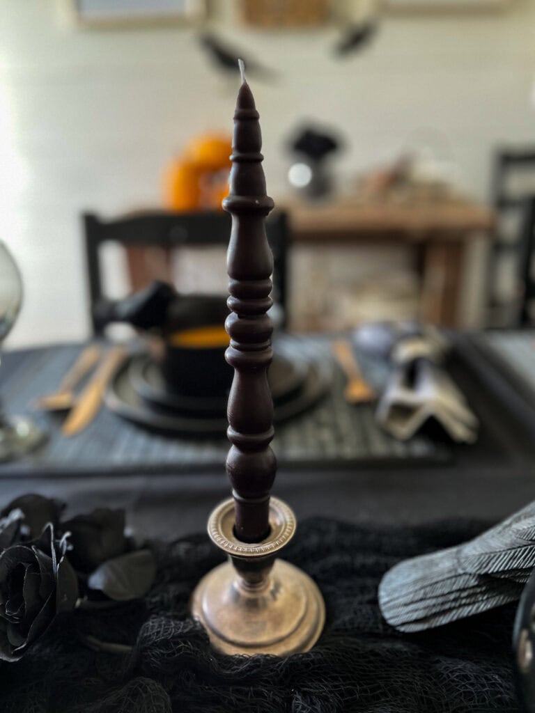 A black taper candle shaped like a spindle in a silver candle holder.