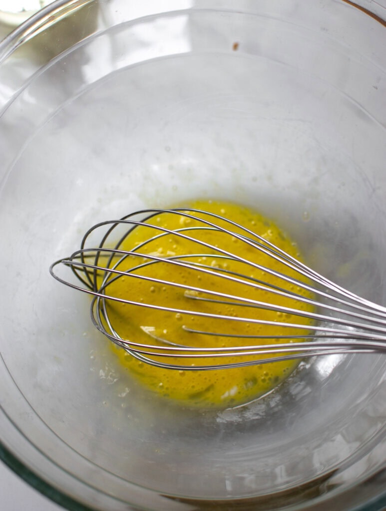 A beaten egg in a glass bowl with a balloon whisk.