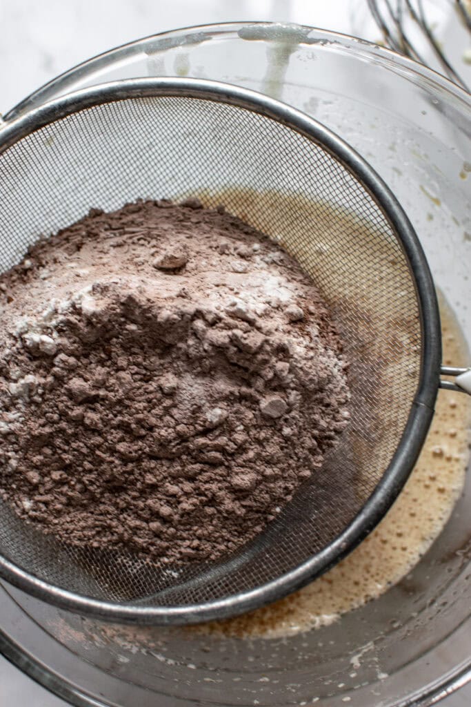 Cocoa powder and all purpose flour being sifted into a mixing bowl with liquid ingredients for cupcakes.