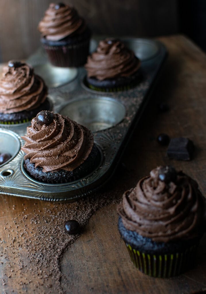 A cupcake tin with frosted chocolate coffee cupcakes, each topped with a coffee bean and grated chocolate.