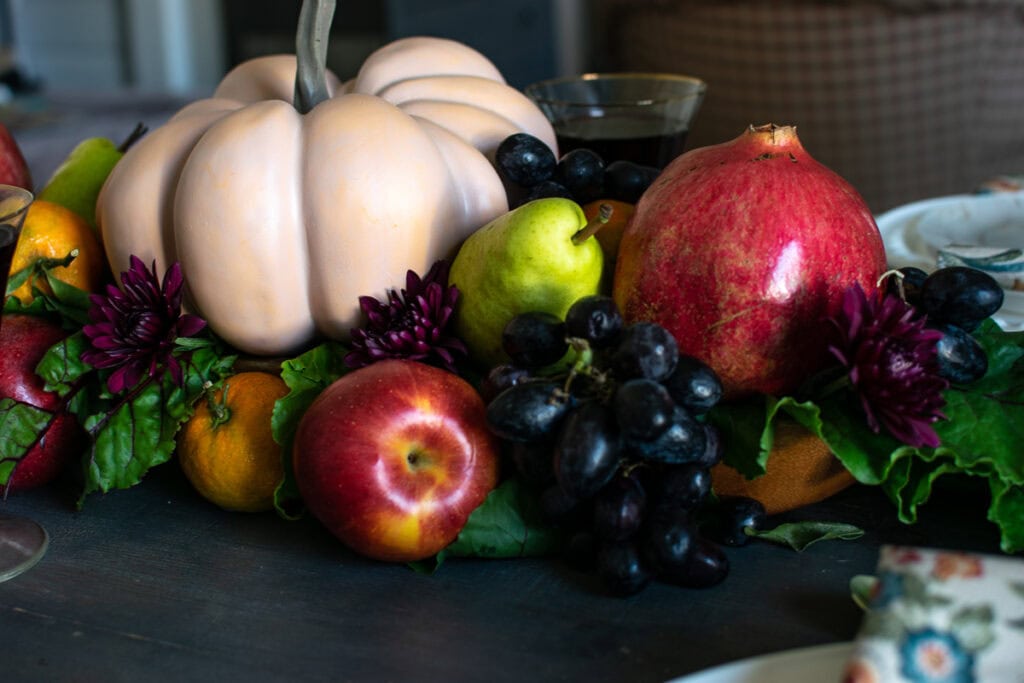 A close up of a fresh fruit centrepiece with a faux orange pumpkin in the centre.