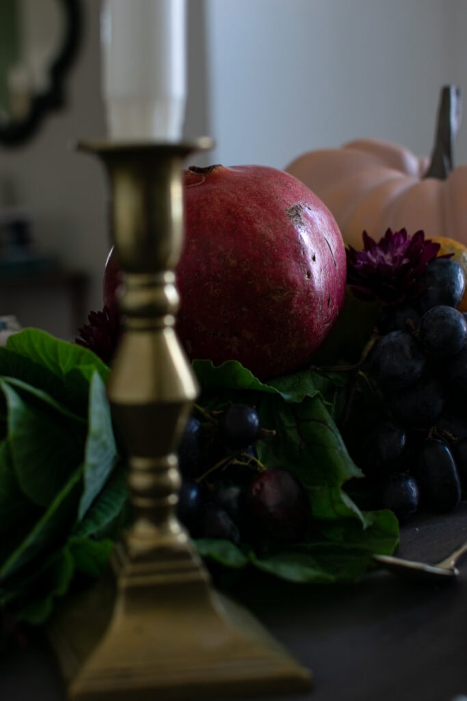 A very close up photo of a gold candlestick with a white candle in it, and a pomegranate in the background.