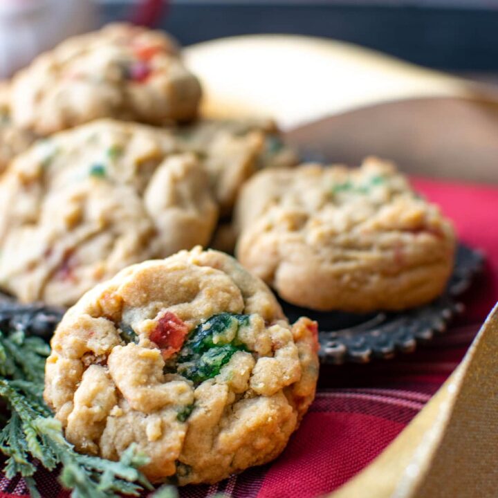 A close up of a green and red candied cherry cookie on a red plaid napkin.