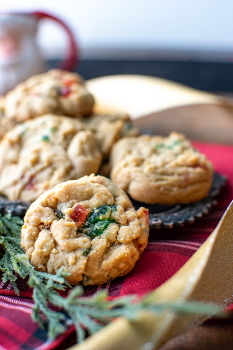 A close up of a green and red candied cherry cookie on a red plaid napkin.