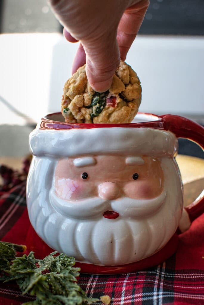 A cherry cookie being dunked into milk that is in a Santa Claus mug.