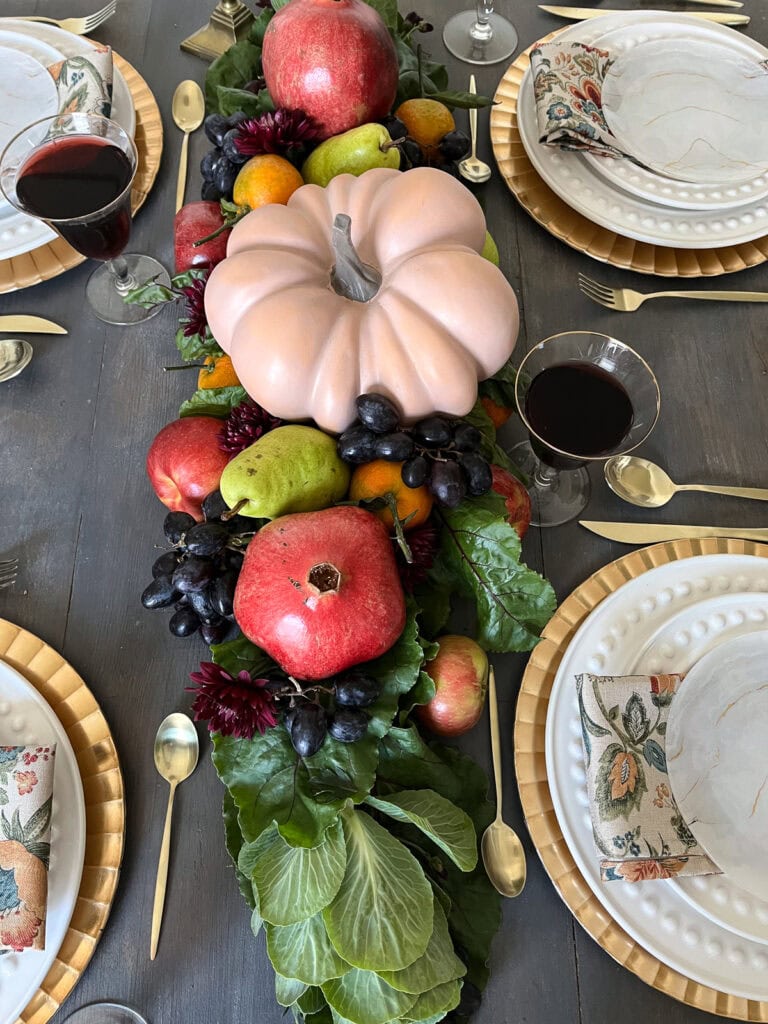 Overhead view of a table runner created with fresh beet greens, fresh fruit and a faux pumpkin.