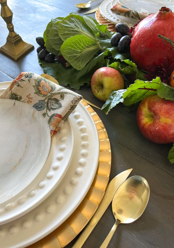 The corner of a stack of plates on a gold charger plate set on a Thanksgiving table.