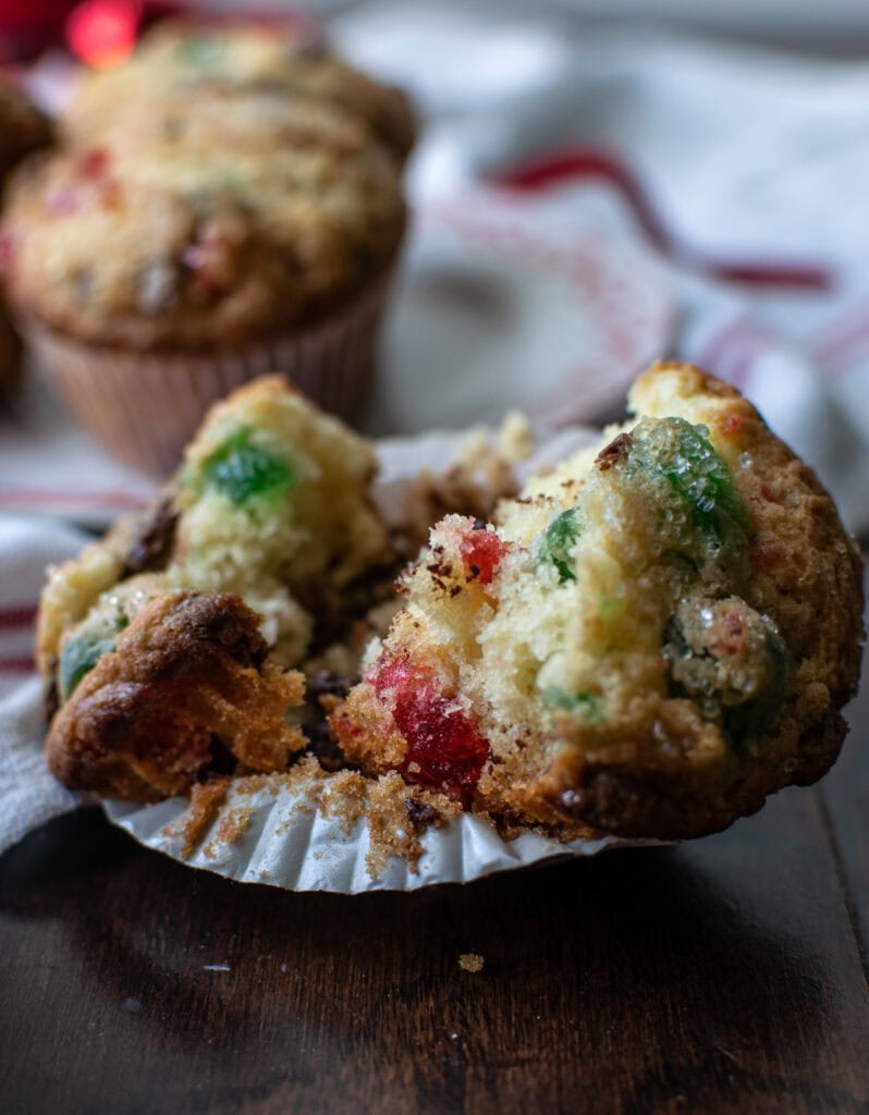 A cherry chocolate chip muffin torn in half sitting on the paper muffin cup.