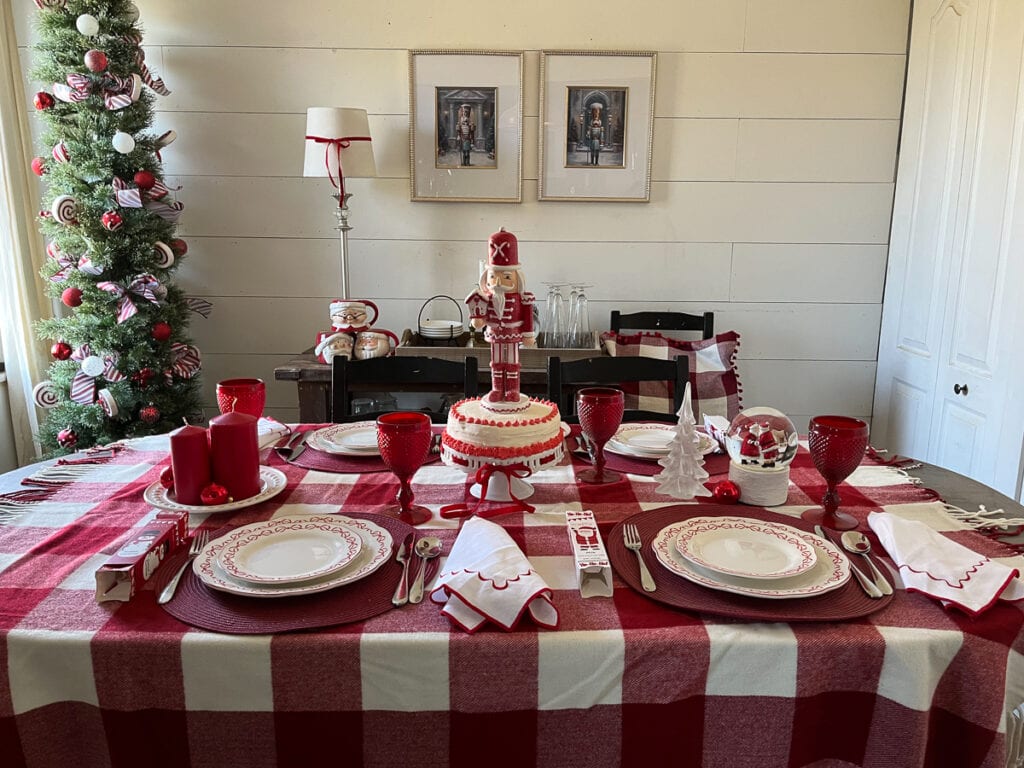 A overhead view of a red and white Christmas dinner table decorated with red and white checked tablecloth, red wine glasses and white plates with red bows.