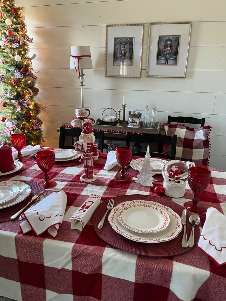 A dinner table set for Christmas in all red and white.  A red and white check table cloth, red water glasses, white china with red bows around the rim.