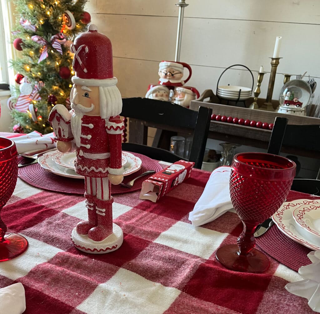 Red and white nutcracker on a table set for Christmas dinner.