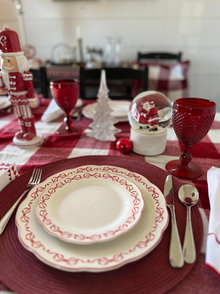 A snow globe with Santa and Mrs. Claus inside beside a frosted glass Christmas tree on a dinner table.