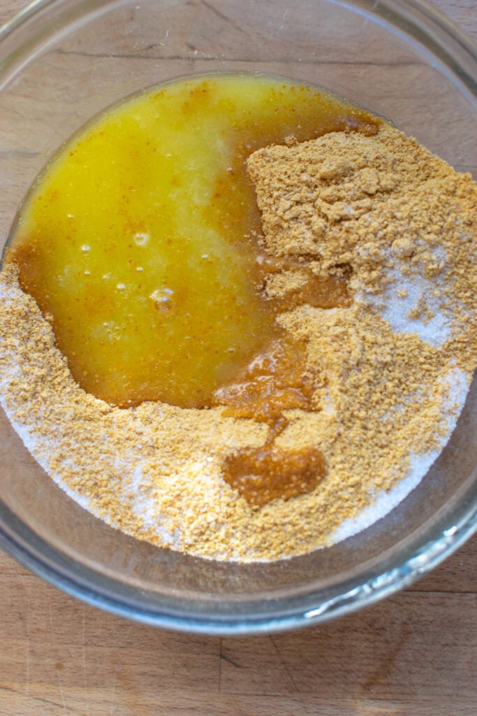 Graham cracker crumbs, melted butter and sugar in a mixing bowl before being mixed together.