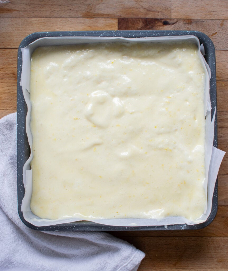 Filling for lemon squares poured over graham cracker crust in a square baking pan.