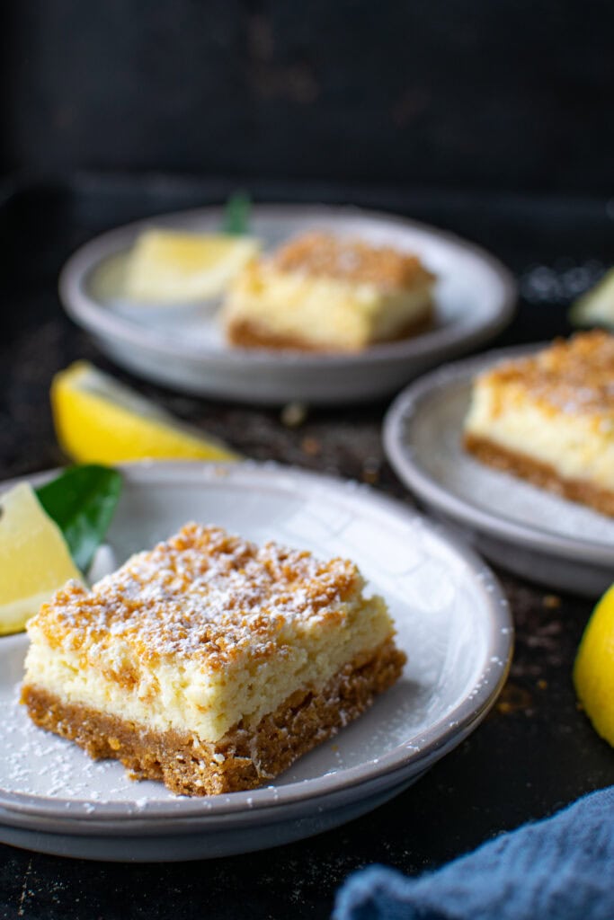 3 plates each with one Lemon squares with graham cracker crust and topping, and lemon slices between each plate.