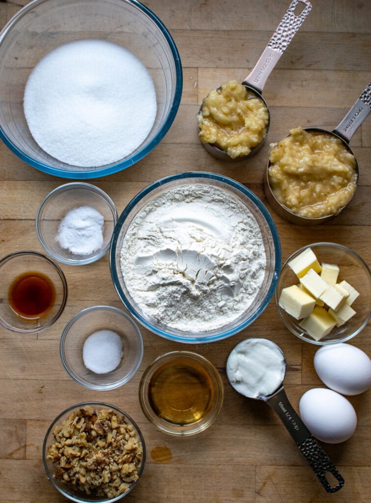 All the ingredients needed to make banana bread with rum including flour, sugar, bananas, eggs, butter, baking soda and yogurt.