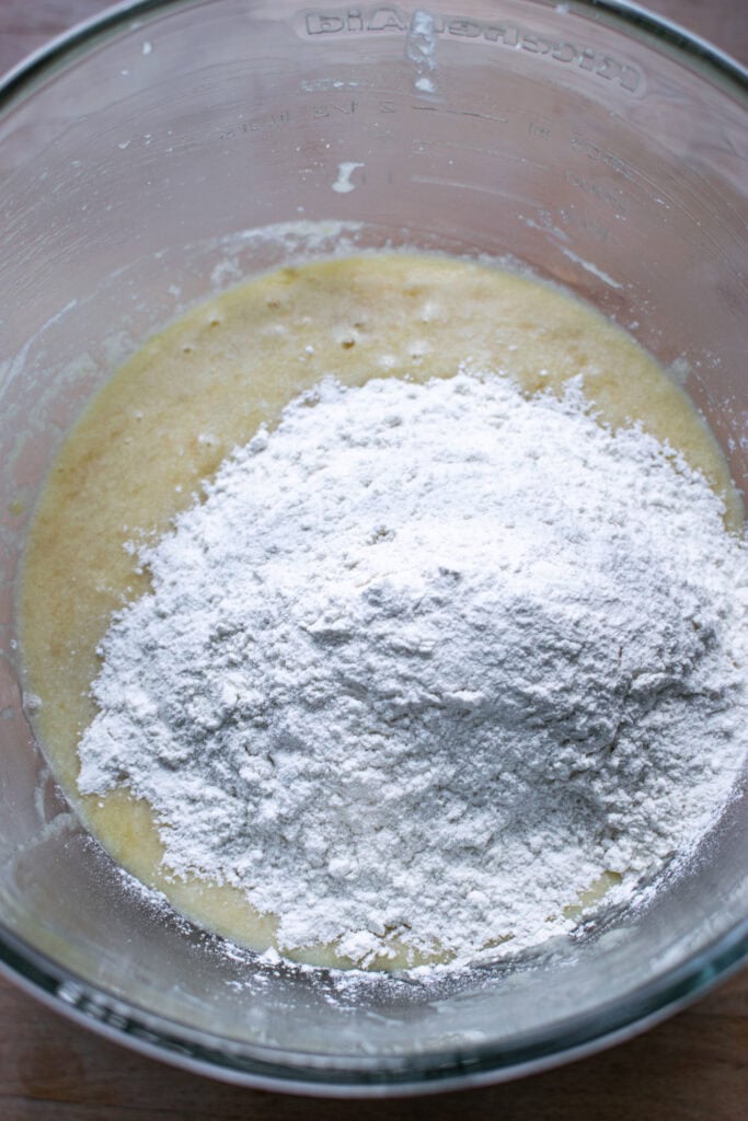 Dry ingredients for banana bread added to the wet ingredients in a glass bowl, before being mixed in.